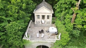 A small, white, two-story building with a central staircase, surrounded by lush greenery. - The Boathouse, Orchardleigh Estate
 (Frome)
