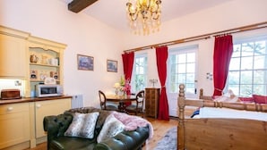 A cozy room with a wooden bed, a leather sofa, a dining table, and a kitchen area. - The Boathouse, Orchardleigh Estate
 (Frome)