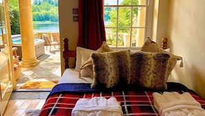 A bedroom with a bed, pillows, a red plaid blanket, and a view of a pool and greenery. - The Boathouse, Orchardleigh Estate
 (Frome)