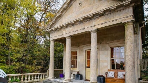 A classical building with a portico supported by columns, a wooden bench, and a small table with a cushion. - The Boathouse, Orchardleigh Estate
 (Frome)