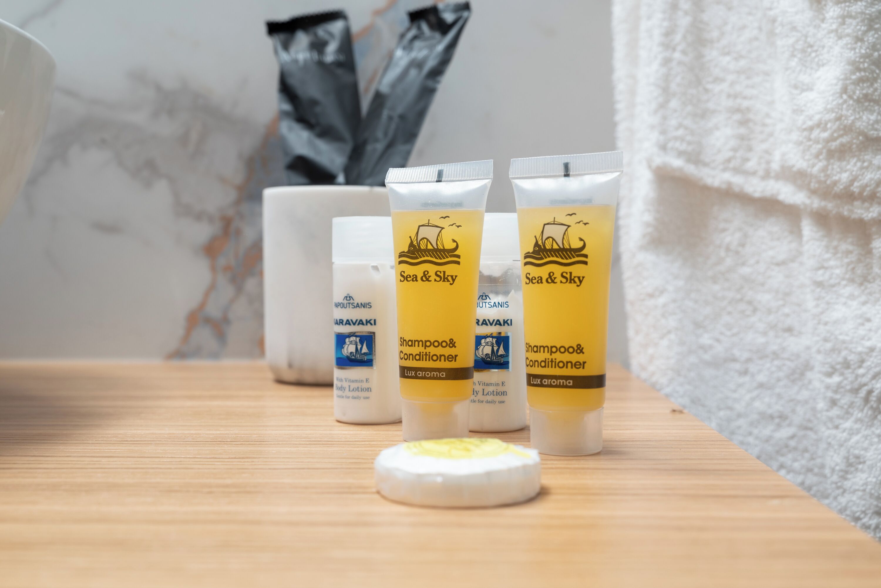 Un bagno con un mobile lavabo in legno, un asciugamano bianco e tre flaconi di shampoo e balsamo Sea & Sky.
