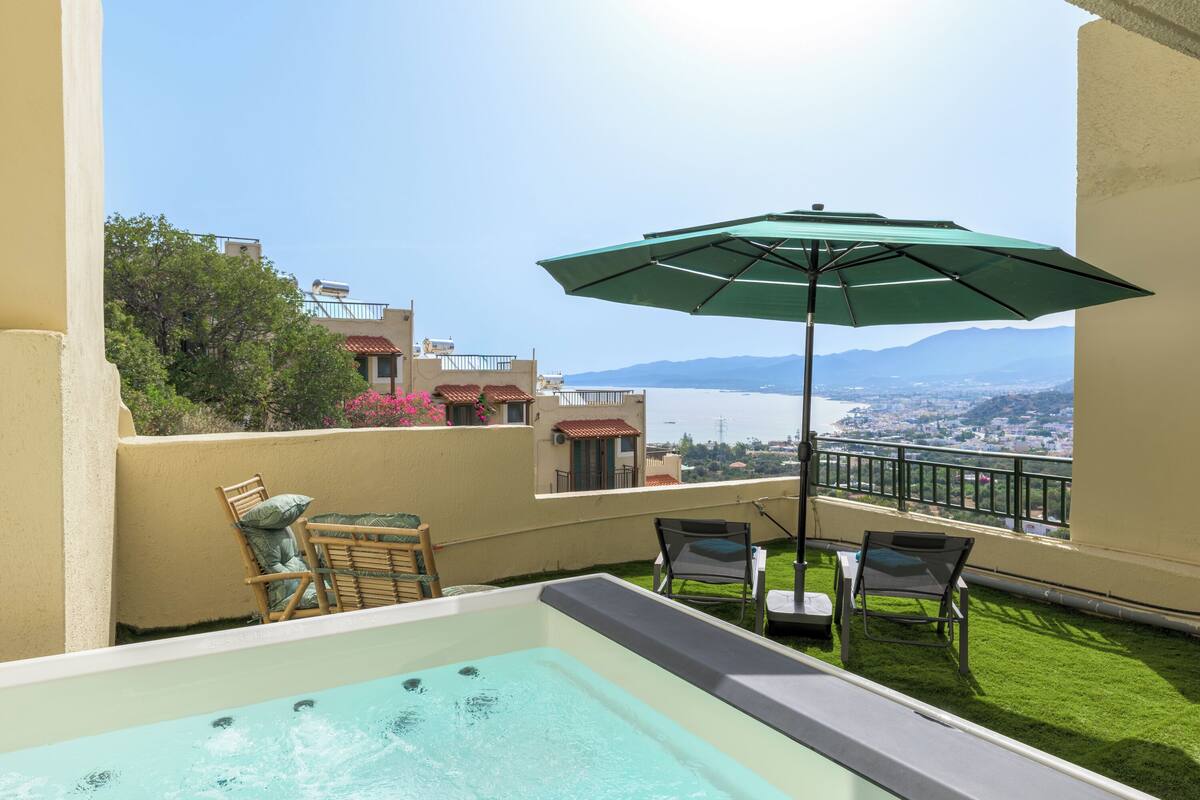 A rooftop terrace with a hot tub, outdoor seating, and a view of the city and mountains.