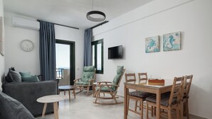 Un saló modern amb un sofà gris, cadires d'oscil·lació de fusta, una taula de dinar amb cadires, una taula rodona petita i un televisor penjat a la paret.