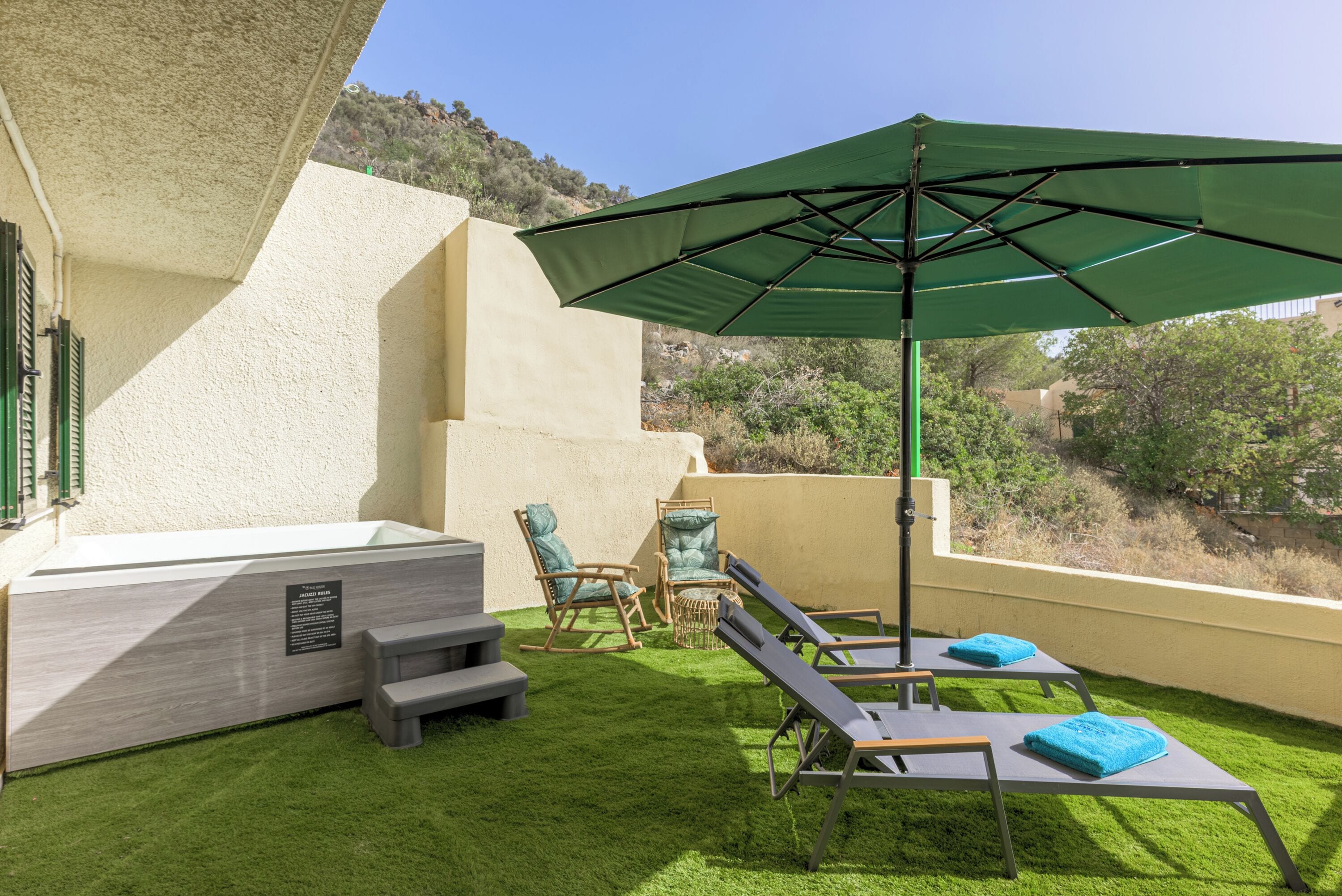 A rooftop terrace with a green umbrella, two lounge chairs, a small table, and a hot tub.