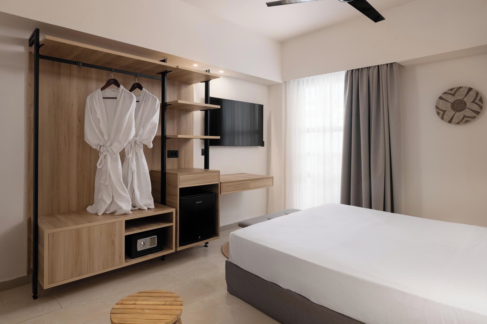 A modern hotel room with a bed, a wooden wardrobe with a TV, and a small table.