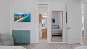 A modern hotel room with a large window, a teal cabinet, a bed, and a bathroom visible through an open door. - Modern Ground flr Condo 1/2 Block to Beach w Pool! (South Padre Island)