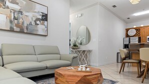 A modern living room with a light grey sofa, a wooden coffee table, and a dining area with wooden chairs. - Modern Ground flr Condo 1/2 Block to Beach w Pool! (South Padre Island)
