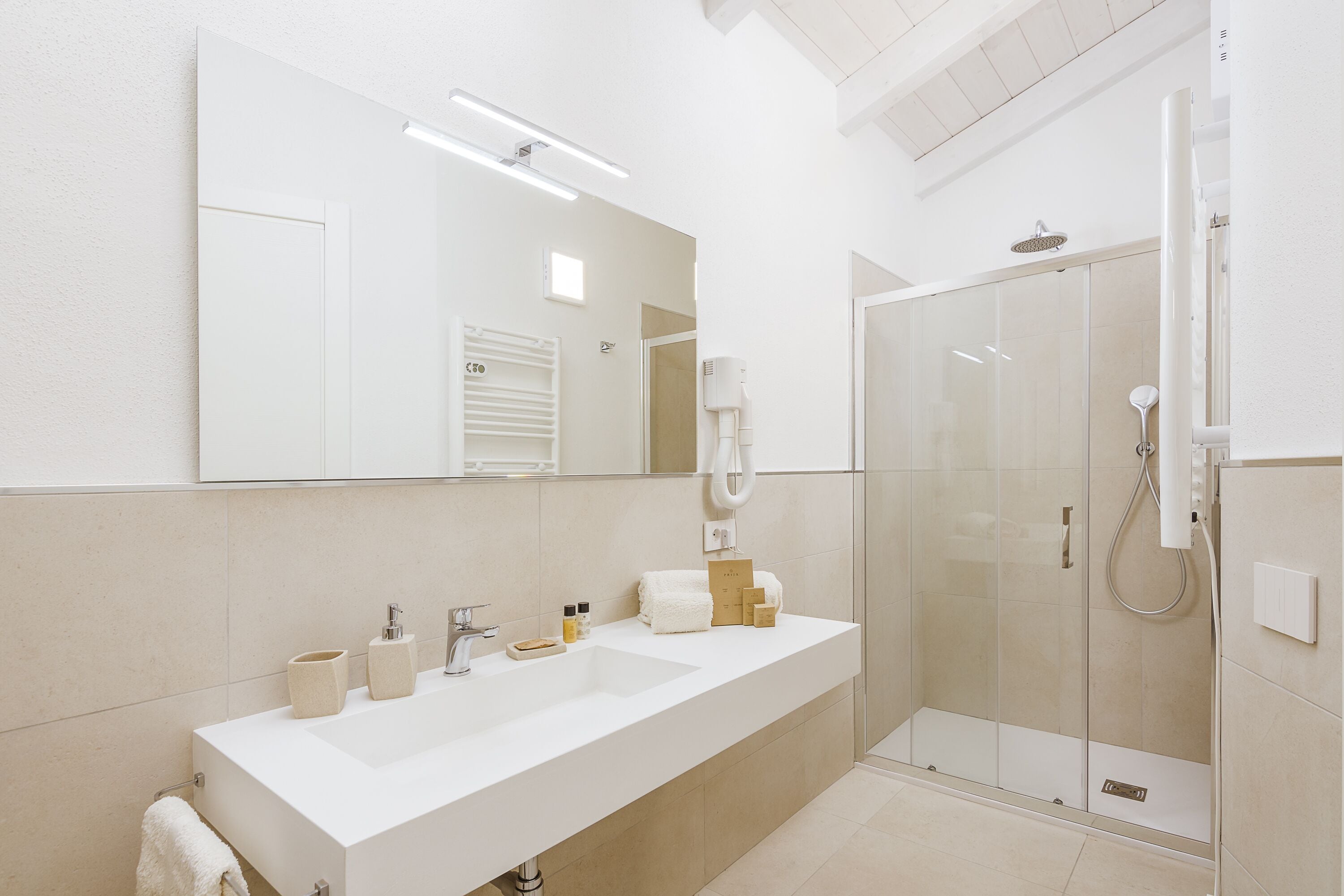 A modern bathroom with a large mirror, a white sink, and a glass-enclosed shower.