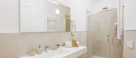 A modern bathroom with a large mirror, a white sink, and a glass-enclosed shower.