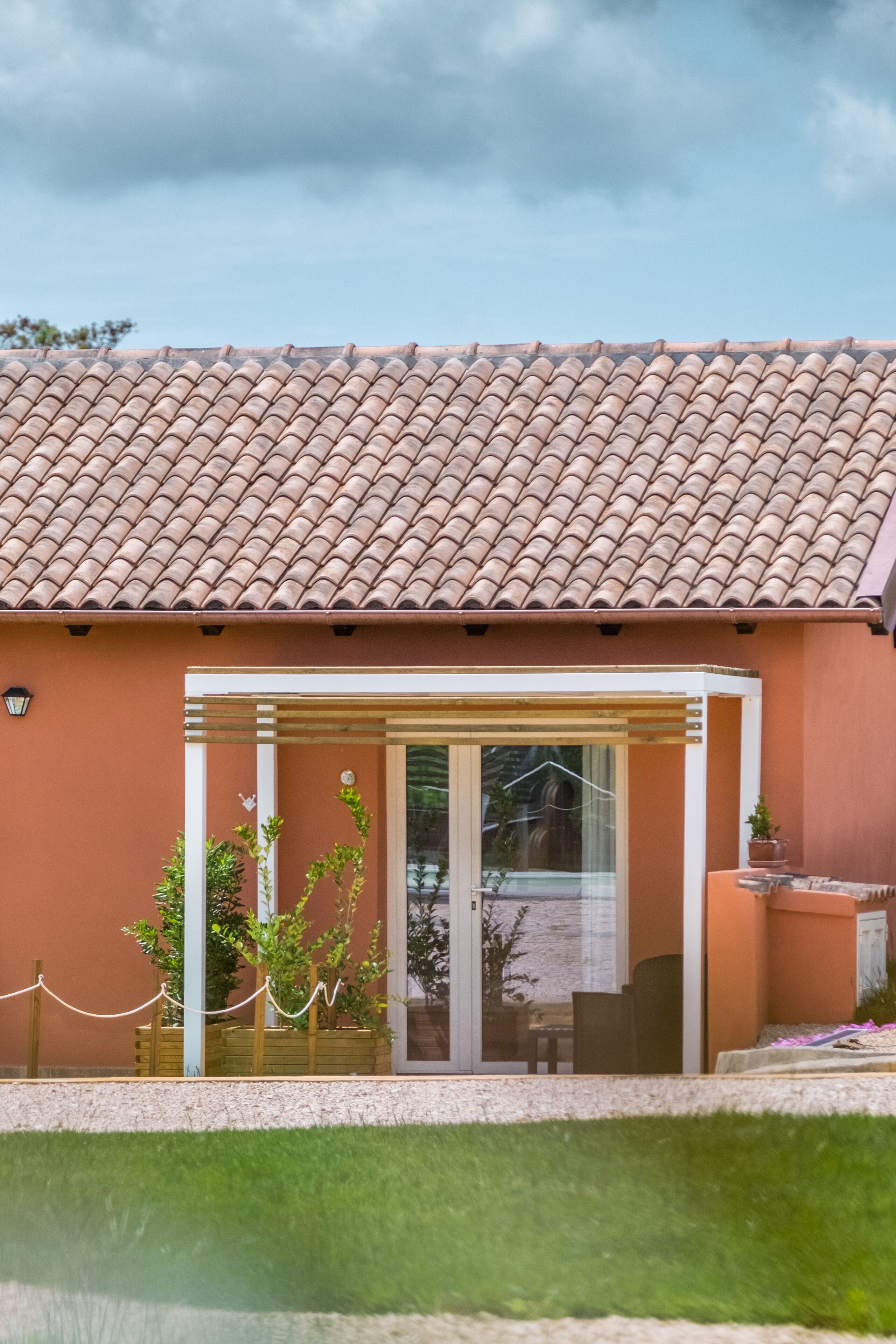 A house with a tiled roof, a glass door entrance, and a small garden area.