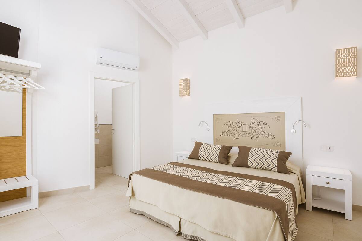 Un dormitorio con cama, mesitas de noche, armario y una puerta que da a un baño.
