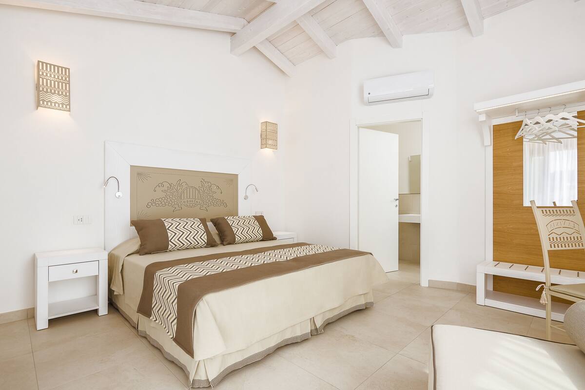 Un dormitorio con cama, mesitas de noche, armario y un banco.