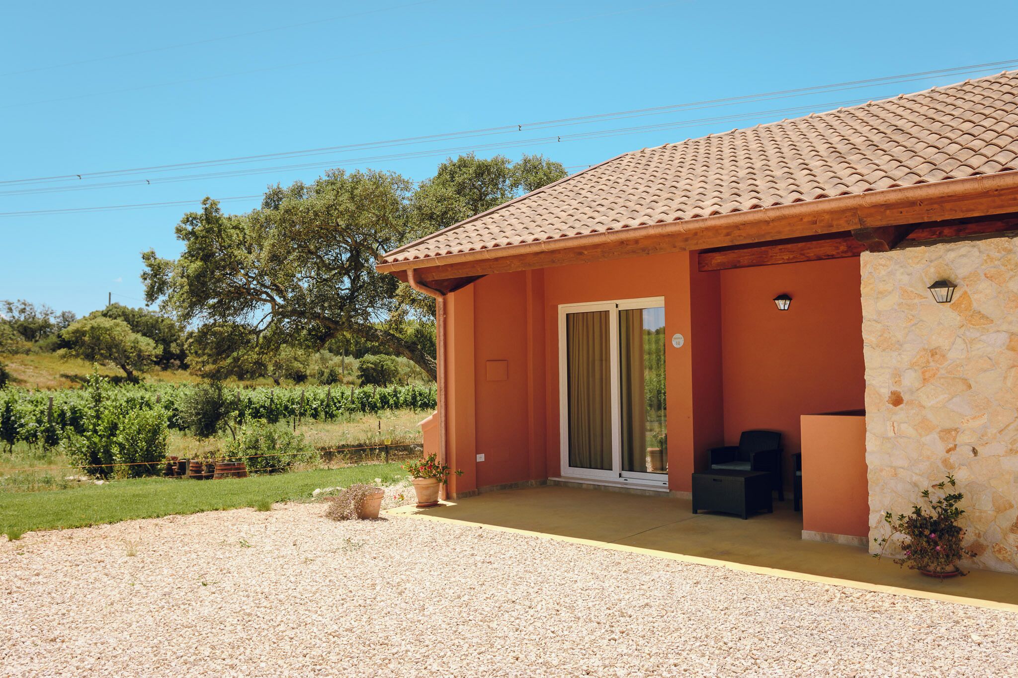 Una casa con techo de tejas, un porche cubierto y un muro de piedra.