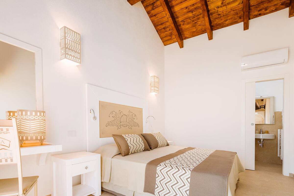 Un dormitorio con techo de madera, una cama con ropa de cama estampada, lámparas de noche y una mesita de noche.