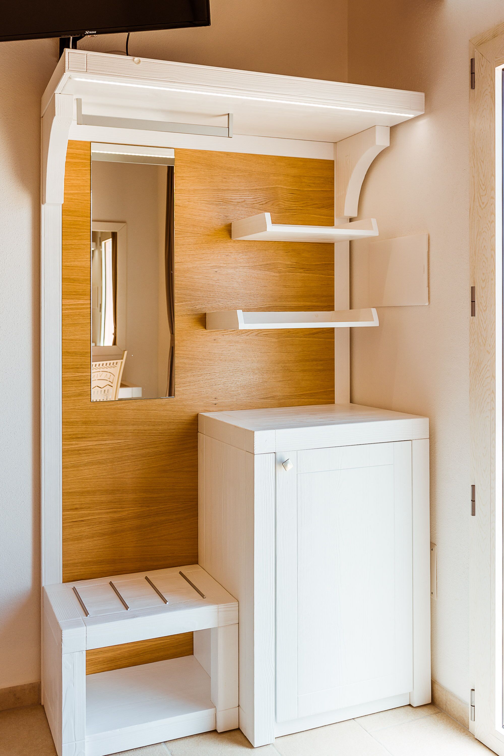 Una habitación pequeña y blanca con tocador incorporado, pared de paneles de madera y un espejo.