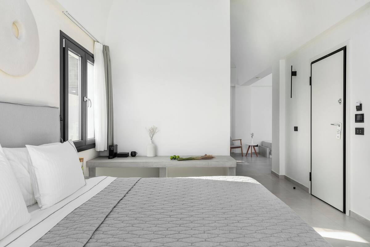 A modern bedroom with a large bed, a bedside table, a window with curtains, and a door.