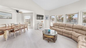 A spacious living room with a dining table, a sofa, and a ceiling fan. - 3BR Beach Condo: : Private Balcony & Pool Access (South Padre Island)