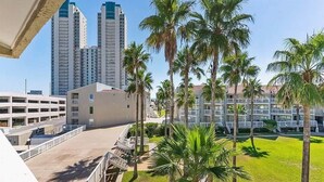 A hotel with a parking garage, palm trees, and high-rise buildings in the background. - 3BR Beach Condo: : Private Balcony & Pool Access (South Padre Island)