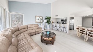 A modern living room with a sectional sofa, a glass coffee table, and a kitchen area with bar stools. - 3BR Beach Condo: : Private Balcony & Pool Access (South Padre Island)