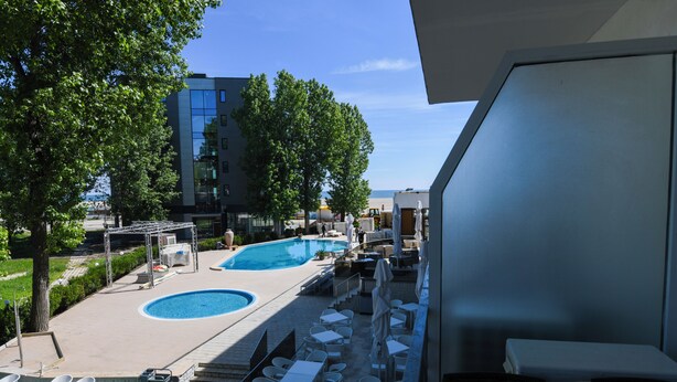 A pool area with two pools, outdoor seating, and a view of a modern building. - Complex Modern Mamaia All Inclusive (Constanta)