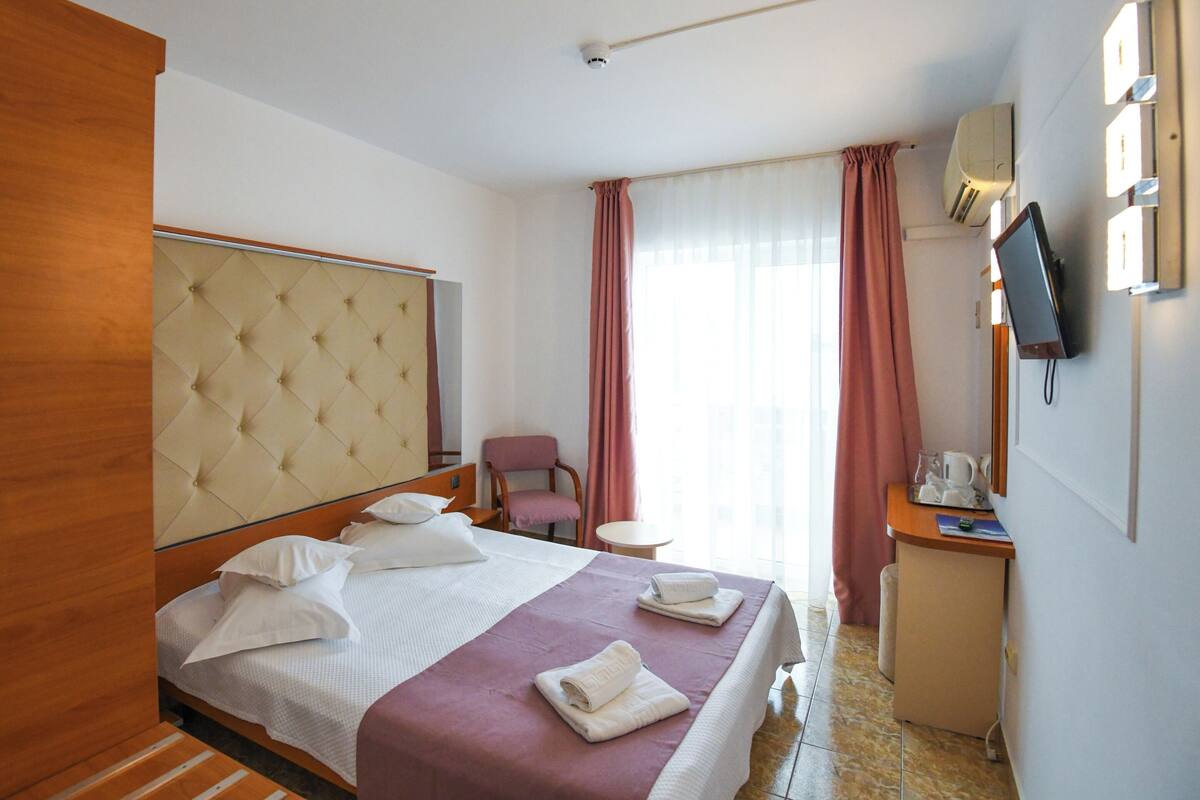 Une chambre d’hôtel avec un grand lit, une chaise, un bureau avec un ordinateur et un téléviseur.
