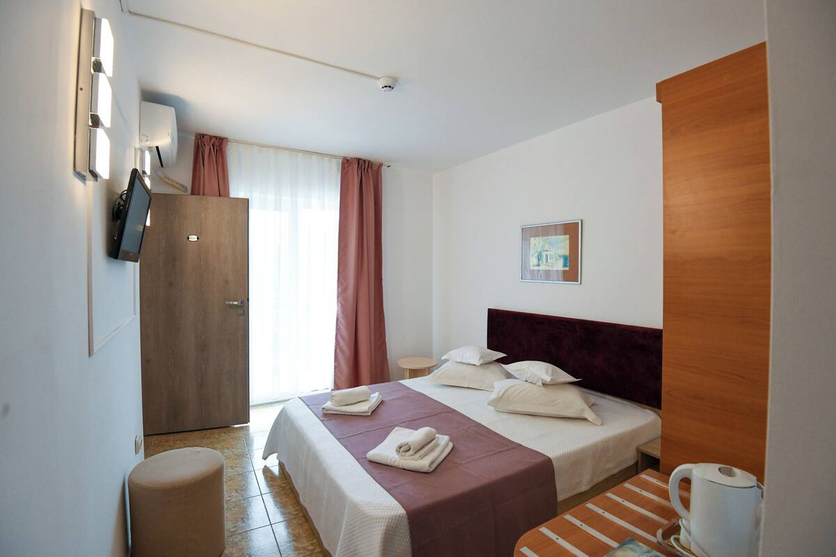 Une chambre d’hôtel avec un lit, un bureau, une chaise, une télévision et une fenêtre avec des rideaux.
