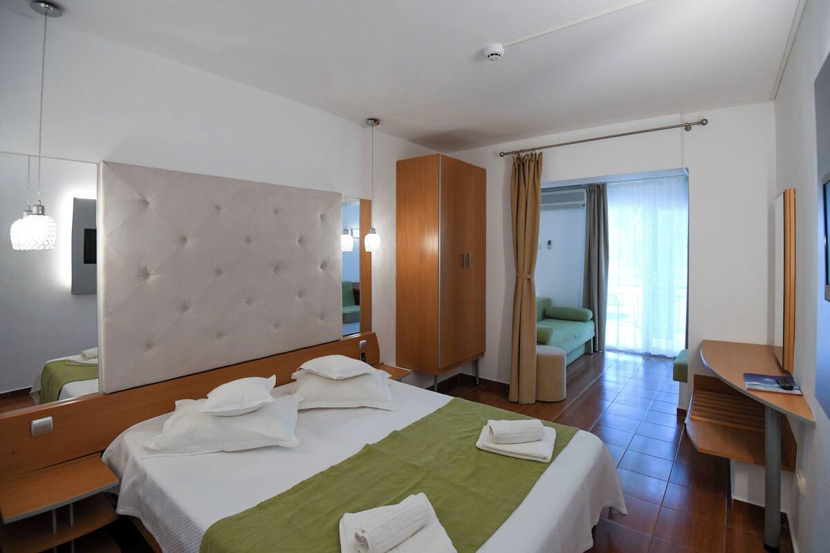 Une chambre d’hôtel comprenant un grand lit, un bureau, une chaise, une armoire et une salle de bain avec douche et toilettes.