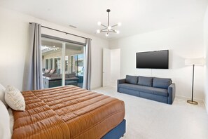 Een slaapkamer met een bed, een bank, een televisie en een schuifdeur met glas.