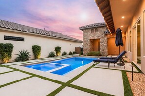 Une piscine au design géométrique, entourée d’une terrasse avec un mur en pierre et un espace salon abrité.
