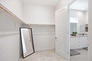 Een moderne badkamer met een grote spiegel, een deur naar een slaapkamer en een douchecel.