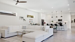 A modern living room with a sectional sofa, a coffee table, and a kitchen area in the background. - Golfers' Paradise: Pool, Spa, EV Charger (La Quinta)