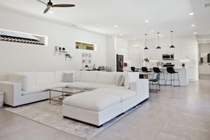 Un salon moderne avec un canapé d’angle, une table basse et un coin cuisine à l’arrière-plan.