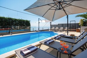 A poolside area with lounge chairs, a table with a drink, and a view of the sea. - Casa Mills, luxury 4 bedrooms house near Opatija (Poljane)