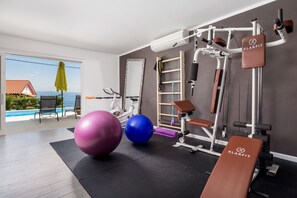 A home gym with exercise equipment, large exercise balls, and a view of a swimming pool and mountains.