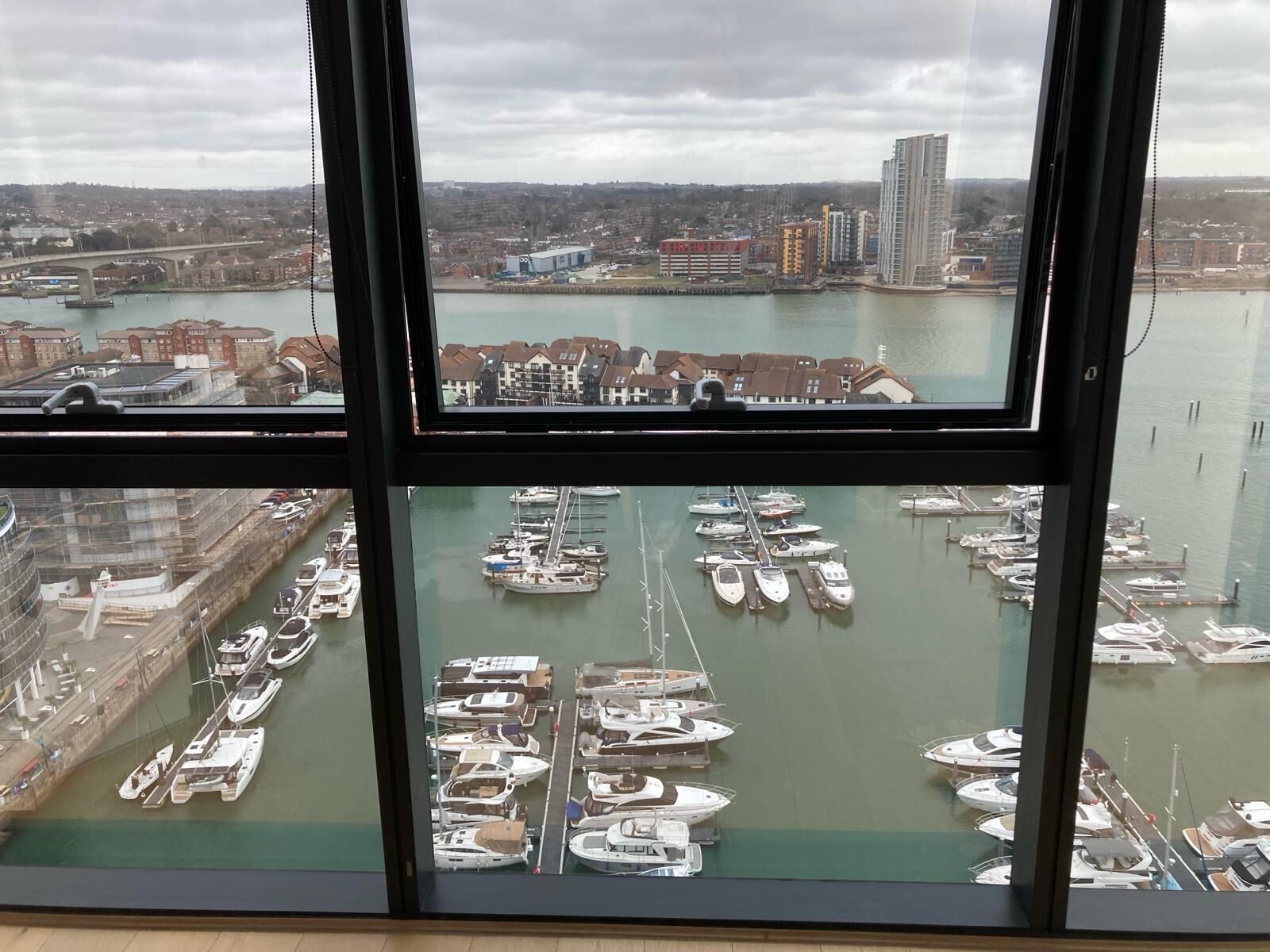 A marina with numerous boats docked, a bridge in the background, and buildings along the waterfront.