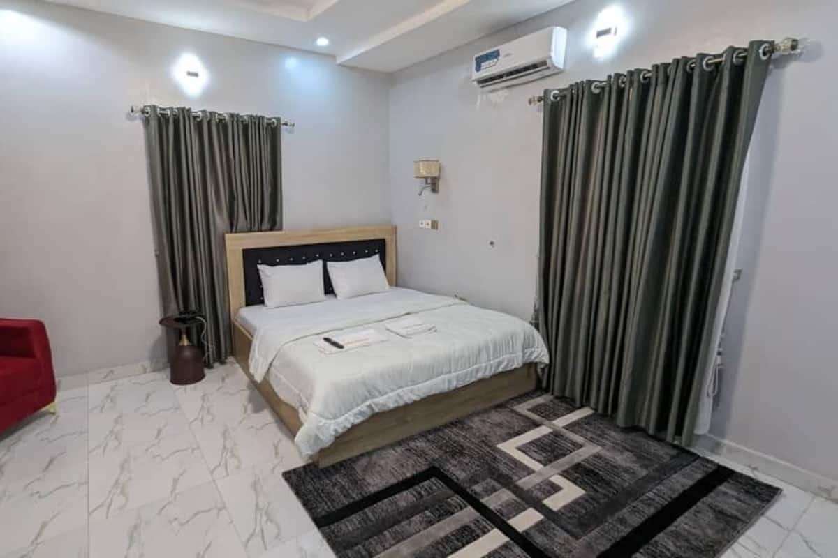 A bedroom with a bed, a red armchair, a patterned rug, and curtains.