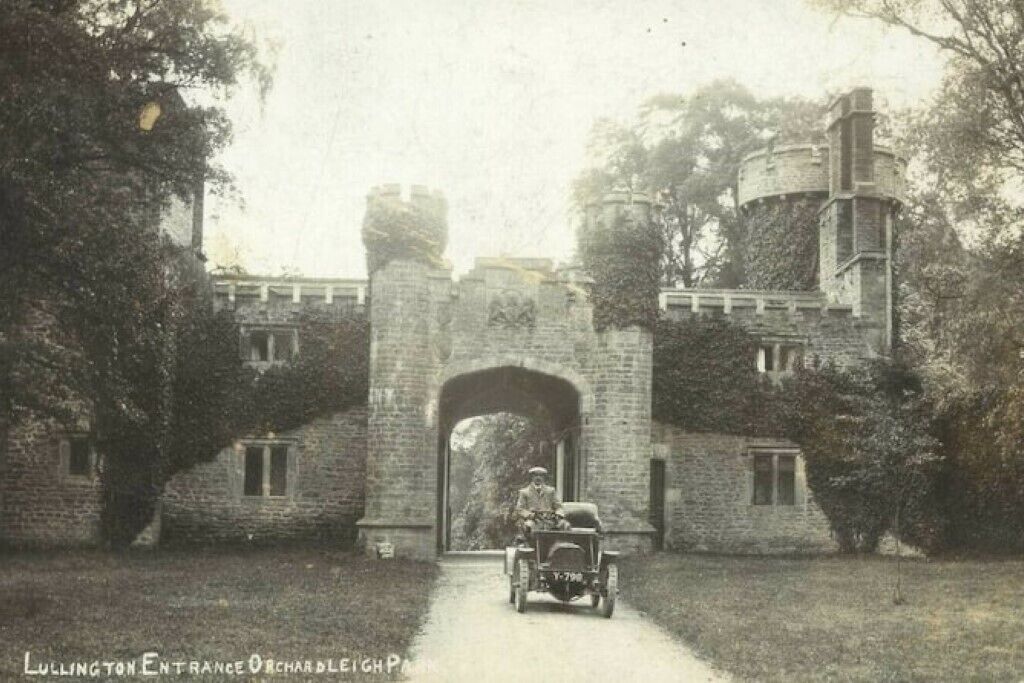 Um edifício histórico com uma grande entrada em arco, uma torre de pedra e um caminho que leva à entrada.