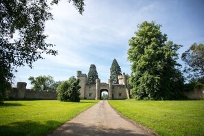 Un château doté d’une arche centrale, entouré de pelouses verdoyantes et luxuriantes ainsi que de grands arbres.