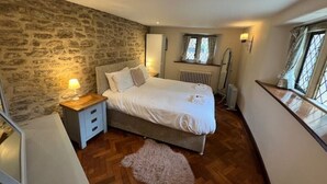 A bedroom with a stone wall, a bed with white bedding, a wooden floor, and a radiator. - Orchardleigh Castle West, Orchardleigh Estate (Lullington)