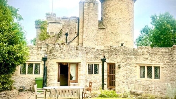 A stone castle with a round tower, a wooden door, and a small garden area with a table and chairs. - Orchardleigh Castle West, Orchardleigh Estate (Lullington)
