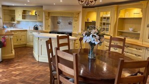 A kitchen with wooden cabinets, a central island, and a dining table with chairs. - Orchardleigh Castle West, Orchardleigh Estate (Lullington)