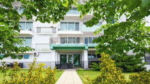 A multi-story building with a green awning, a paved entrance, and a well-maintained lawn with yellow flowering shrubs. - Hotel Romantic (Constanta)