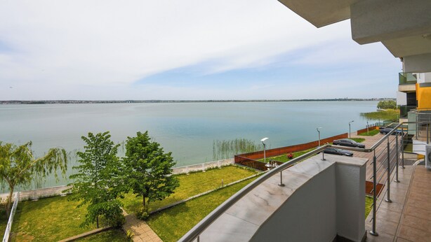 A balcony with a view of a calm lake, a grassy area, and a modern building structure. - Hotel Romantic (Constanta)