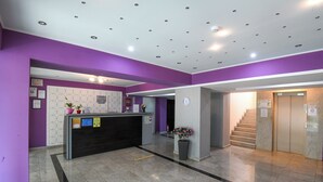 A reception area with a reception desk, a clock, a staircase, and a potted plant. - Hotel Romantic (Constanta)