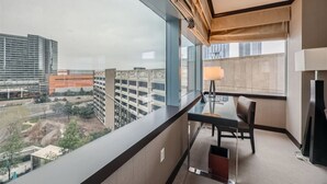 Habitación de hotel con balcón, escritorio, silla y lámpara.