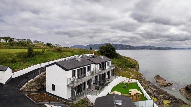 A coastal property with a large balcony overlooking the sea, a grassy area, and a view of distant mountains. -  Pierside Apartments Deluxe Accommodation (Portsalon)