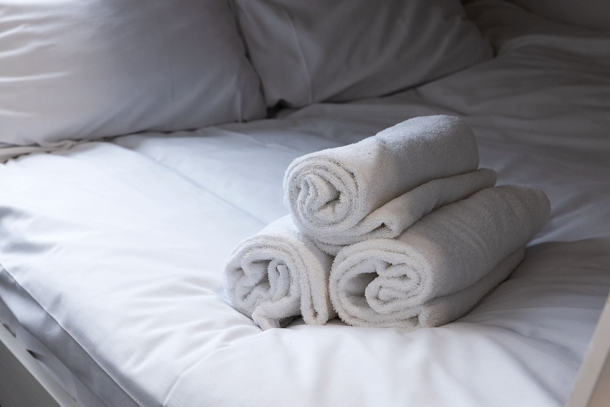 A neatly made bed with white linens and rolled towels.