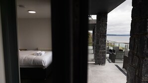 A bedroom with a bed and a view of a balcony with outdoor furniture. -  Pierside Apartments Deluxe Accommodation (Portsalon)