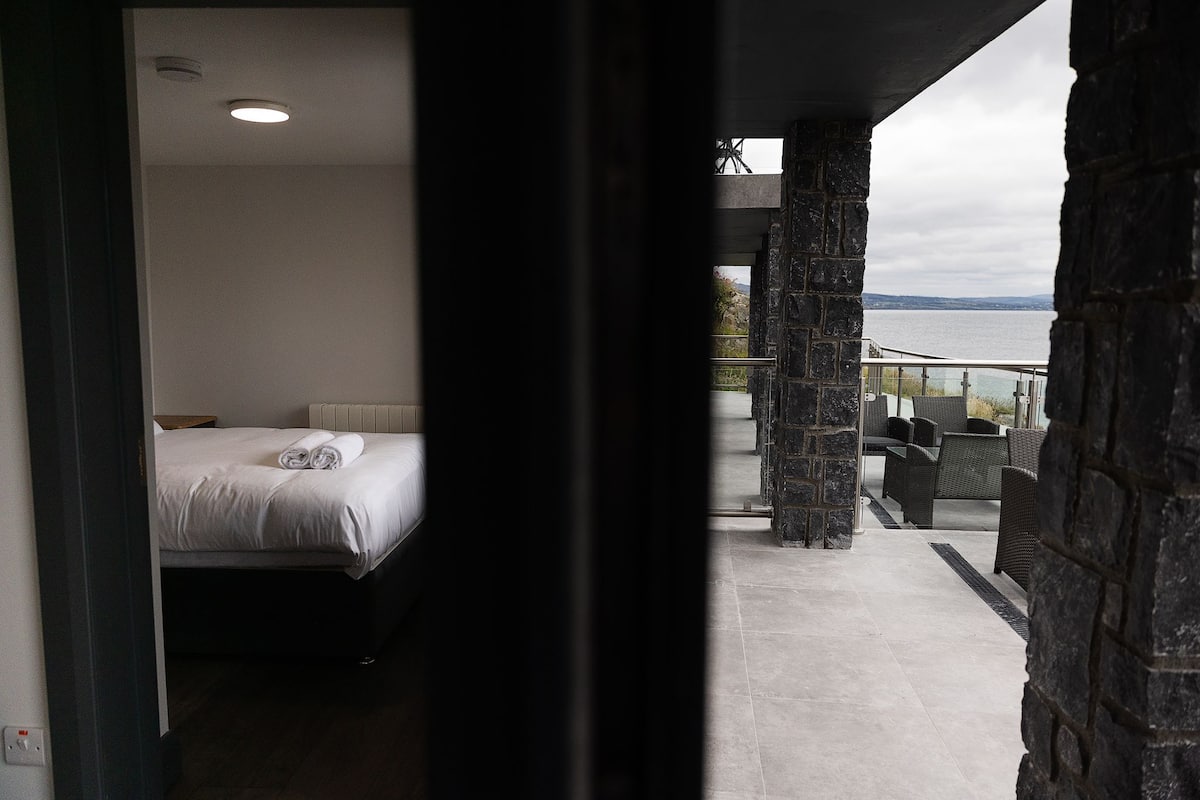Une chambre à coucher avec un lit et une vue sur un balcon aménagé avec du mobilier d’extérieur.