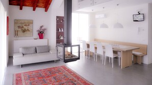 A modern living room with a white sofa, a glass fireplace, a dining area with a wooden table and white chairs, and a red patterned rug. - Ca' Belvedere B&B (Silea)